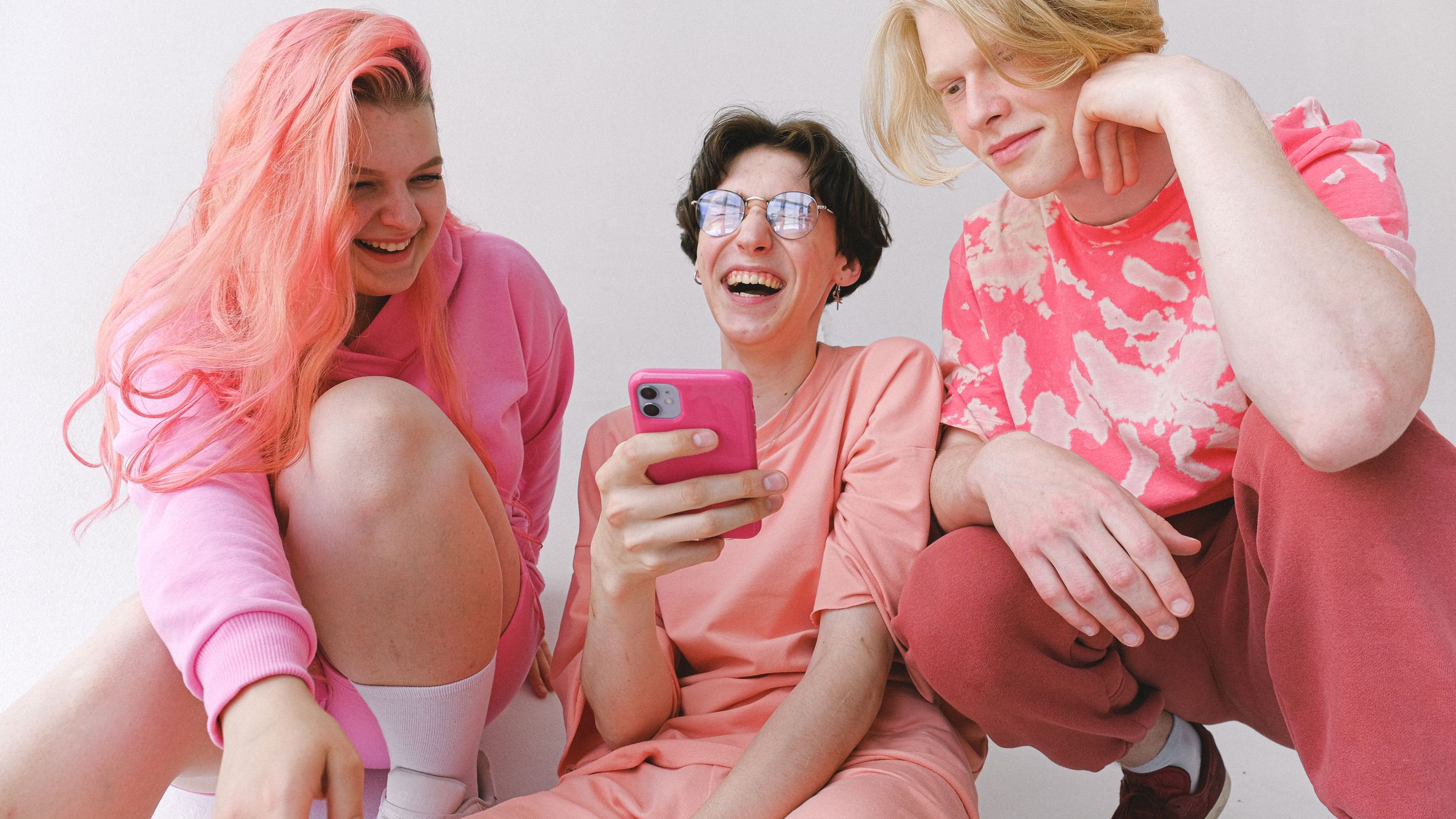 Three friends in pink laughing together while looking at a phone